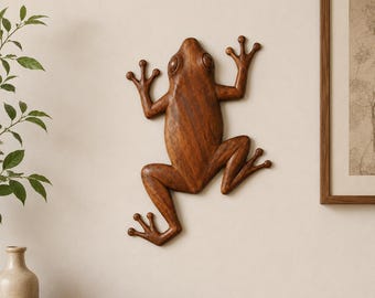 May include: A wall-mounted frog sculpture carved from dark brown wood with a smooth, polished finish. The frog is depicted in a climbing position with four splayed limbs, visible eyes, and a rounded body shape, showcasing natural wood grain patterns.