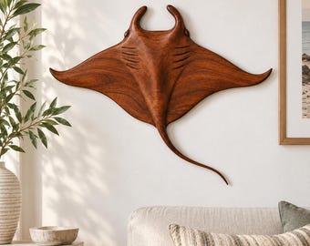 May include: A wall-mounted manta ray sculpture carved from dark brown wood with a visible grain pattern. The piece features a wide wingspan, a long slender tail, and carved gill slits on the dorsal side, displaying a smooth, polished finish.