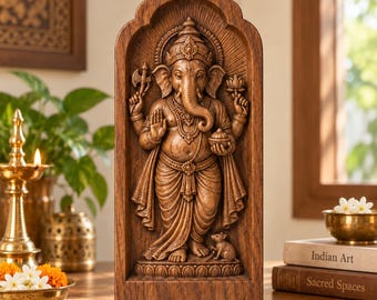 May include: A brown wooden sculpture of the deity Ganesha, depicted with an elephant head and four arms, standing within an arched frame. The figure holds an axe and a lotus flower, with a small mouse positioned at the feet on a base.
