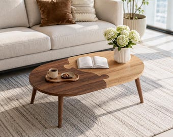 May include: A coffee table featuring a two-tone design with a dark brown wood side and a light brown wood side that interlock like a puzzle piece. The table has four tapered wooden legs and holds an open book, a small tray with nuts, and a white vase.