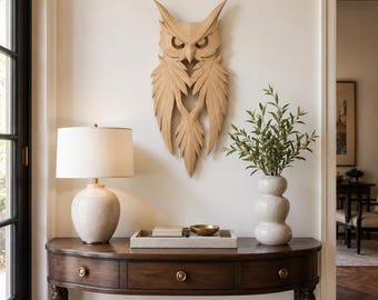 May include: A light-colored wooden owl wall sculpture with sharp, angular feather details and pointed ears. The owl is mounted on a plain wall above a dark wood semi-circular console table featuring three drawers with small round brass knobs.