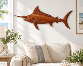 May include: A wall-mounted wooden marlin sculpture featuring a rich brown finish, detailed carved fins, a long pointed bill, and a curved tail. The fish is depicted in a horizontal swimming position with visible wood grain texture throughout the body.