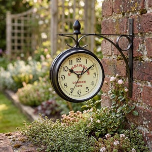 Puede incluir: Un reloj de estación de pared de metal negro con una esfera de color crema. El reloj presenta números arábigos negros, manecillas negras y texto rojo que dice Kensington Station London 1879. Está sujeto a un soporte de metal negro decorativo.