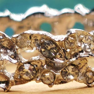 May include: A silver-toned metal ring featuring a textured, organic, branch-like design. The band is encrusted with numerous small, clear, round-cut stones that are embedded throughout the irregular, jagged surface of the metal structure.