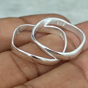 May include: Two interlocking square-shaped silver rings with a polished finish. The inner band of one ring is clearly stamped with the hallmark 925, indicating sterling silver composition. The rings feature smooth, rounded edges and a reflective surface.