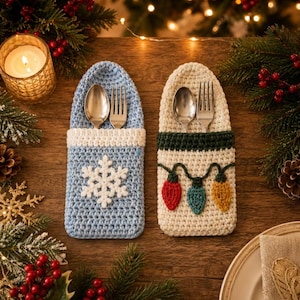 May include: Two crochet silverware holders. The left holder is light blue with a white snowflake applique. The right holder is cream with a dark green band and a string of red, teal, and yellow crochet Christmas light bulb appliques.