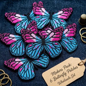 May include: A set of six embroidered butterfly patches featuring vibrant blue and pink wings with black outlines. The patches are arranged together with a tan paper tag that reads: Makers Pack: 6 Butterfly Patches Wholesale Set.