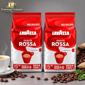 Könnte beinhalten: Zwei rote Packungen Lavazza Qualità Rossa ganze Kaffeebohnen, jeweils 1 kg schwer. Die Verpackung zeigt eine rote Kaffeetasse, den Text "Medium Roast" und eine Intensitätsbewertung von 5/10. Kaffeebohnen sind um die Packungen verstreut.