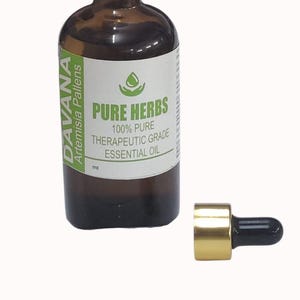 Puede incluir: Un frasco de vidrio marrón de aceite esencial de Davana Artemisia Pallens con tapa blanca y una etiqueta que dice Pure Herbs 100% Pure Therapeutic Grade Essential Oil. Un gotero dorado con una perilla de goma negra se encuentra al lado.