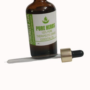 Pode incluir: Um frasco de vidro castanho com tampa branca e um rótulo branco com a inscrição PURE HERBS 100% PURE THERAPEUTIC GRADE ESSENTIAL OIL e CITRONELLA JAVA Cymbopogon winterianus. Um conta-gotas com colar dourado está à frente.