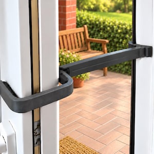 Può includere: Una barra di sicurezza in metallo nero installata orizzontalmente su un telaio di porta bianco. Il dispositivo presenta una maniglia a forma di U sul lato sinistro che si collega a una barra di bloccaggio dritta che si estende verso il lato destro.
