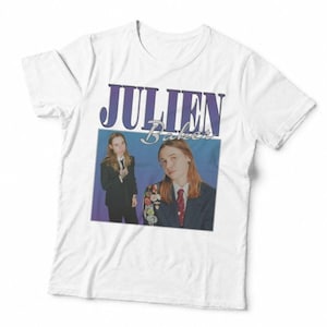 May include: A white short-sleeved t-shirt featuring a graphic print of the musician Julien Baker. The design includes the name JULIEN in large purple letters above the word Baker in script, with two images of the artist wearing a dark suit.