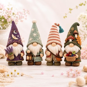 May include: Four crocheted gnome figurines standing in a row. The first wears a purple hat with moon and moth embroidery, holding lavender. The second is in a sage green hat with snowflake embroidery, holding a lantern. The third has a striped hat with a tassel, and the fourth wears a dark green hat with mushroom and leaf appliqués, holding a basket of berries.