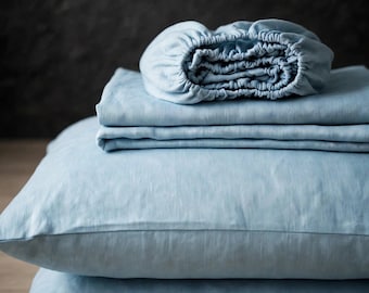 Può includere: Un set di biancheria da letto azzurro composto da un lenzuolo con angoli elasticizzati, un lenzuolo piano piegato ordinatamente e due federe rettangolari impilate. Il tessuto presenta una trama visibile in un colore blu tenue e uniforme.