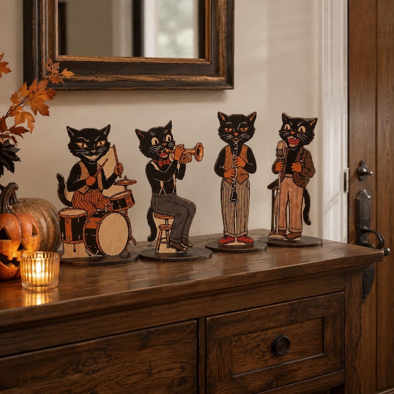 May include: Four freestanding black cat figures arranged in a jazz band formation. One cat plays drums, another plays a trumpet, the third plays a clarinet, and the fourth sings into a microphone. Each cat wears vintage-style clothing on a flat base.