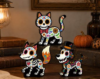May include: Three wooden animal figurines featuring colourful sugar skull patterns. The set includes a cat with a bow tie, a fox with a bushy tail, and a dog wearing a top hat. Each figure is painted with intricate floral and skeletal designs.