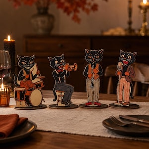 May include: Four freestanding wooden cutouts of black cats dressed in vintage clothing, each playing a different musical instrument including drums, a trumpet, a clarinet, and a microphone, all mounted on circular bases for display.