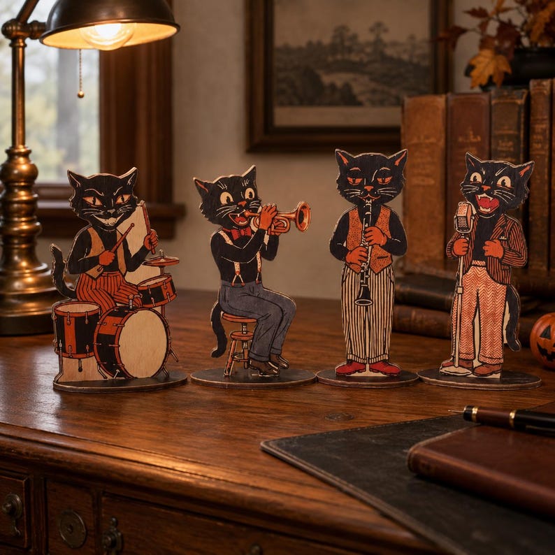 May include: Four freestanding wooden cutouts of black cats dressed in vintage clothing, each playing a different musical instrument including drums, a trumpet, a clarinet, and a microphone, arranged in a row on a dark wooden desk surface.