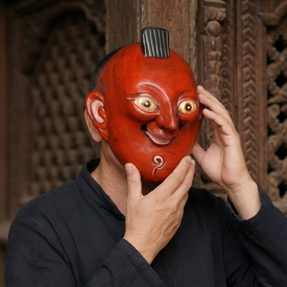A hand-carved wooden smiling mask with genuine folk-art weirdness — the kind of wall piece that stops guests mid-sentence and demands a story.