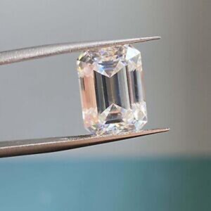 Könnte beinhalten: Ein klarer, farbloser Edelstein im Smaragdschliff mit rechteckigen Facetten, die scharfe geometrische Linien und interne Lichtreflexionen erzeugen. Der Stein wird sicher zwischen den beiden Metallspitzen einer silberfarbenen Pinzette gehalten.