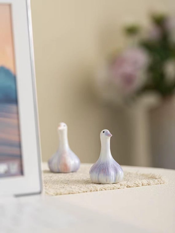 A hand-sculpted porcelain duck wearing a garlic bulb like a hat — chaotic, absurdist, and clearly made by someone with a wonderfully weird imagination.