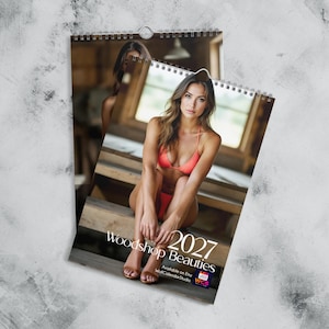 Peut inclure: Un calendrier mural 2027 intitulé Woodshop Beauties présentant une photographie d'une personne en bikini corail assise sur des marches en bois. Le calendrier possède une reliure à spirale blanche en haut et inclut le texte Woodshop Beauties 2027.