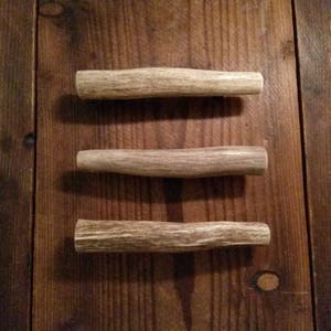 May include: Three antler handles, each with a different shape and size, are arranged in a vertical row on a wooden surface.