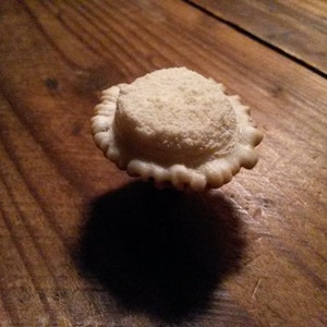 Puede incluir: Una mini tarta redonda, blanca y glaseada con una corteza escamosa sobre una superficie de madera.