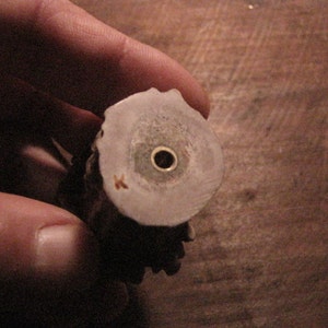 Puede incluir: Primer plano de la parte inferior de un tap&oacute;n de botella de hueso. El tap&oacute;n tiene una peque&ntilde;a inserci&oacute;n de metal en el centro.