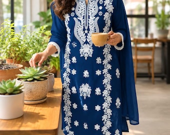 Könnte beinhalten: Eine tiefblaue Tunika mit langen Ärmeln, die entlang des Ausschnitts und der Vorderseite mit aufwendigen weißen Blumenstickereien verziert ist, kombiniert mit einer passenden blauen Hose und einem über die Schultern drapierten Schal.