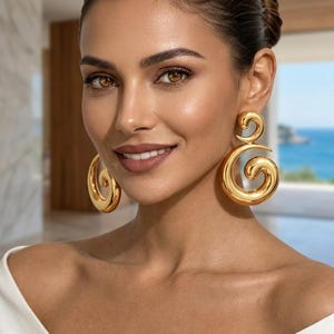 May include: A pair of large, polished gold-tone earrings featuring a double-swirl design. Each earring consists of a smaller circular spiral at the top connected to a larger, thicker circular spiral at the bottom, creating a continuous, smooth, metallic loop structure.