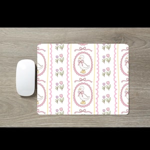 May include: A rectangular mouse pad featuring a repeating pattern of white ducks wearing yellow boots and pink bows, enclosed in pink scalloped oval frames, interspersed with pink tulip illustrations and vertical yellow wavy lines on a white background.