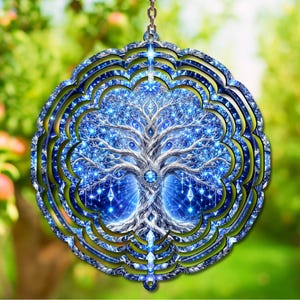 May include: A circular metal wind spinner featuring a detailed tree of life design in shades of blue and white. The artwork displays intricate branches and roots with glowing light effects, surrounded by a decorative scalloped frame and a hanging chain.