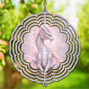 May include: A circular wind spinner featuring a scalloped edge and a central illustration of a pale pink and white dragon with intricate scales and flowing fins. The design is framed by concentric cutouts and hangs from a metal chain.