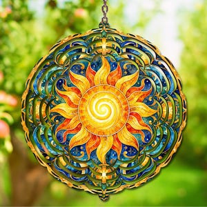 May include: A circular hanging wind spinner featuring a central yellow and orange sun with a spiral core, surrounded by intricate layers of blue and teal celestial patterns with star motifs, suspended by a small metal chain at the top.
