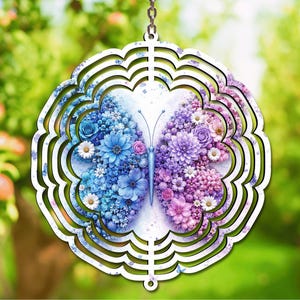 May include: A circular metal wind spinner featuring a butterfly design composed of blue and purple floral patterns. The left wing displays various blue flowers, while the right wing features purple and pink blossoms. A metal chain is attached at the top.