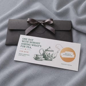 Puede incluir: Una tarjeta de regalo rectangular blanca con un sobre gris oscuro que incluye una cinta de satén. La tarjeta muestra una ilustración de tetera y taza, el texto ONE DAY WITH NOBODY ASKING WHAT'S FOR TEA, FOR MUM, MERRY CHRISTMAS LOVE, BEN X, y un círculo dorado para rascar con la etiqueta SPA DAY & AFTERNOON TEA.