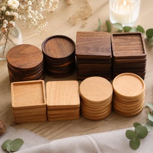 Puede incluir: Una colección de posavasos de madera dispuestos en pilas, con formas circulares y cuadradas. El conjunto incluye posavasos de madera de color marrón oscuro y otros de tonos naturales más claros, todos con superficies lisas y bordes.