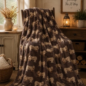 May include: A soft, dark brown plush throw blanket featuring a repeating pattern of light-coloured Highland cattle with long horns and shaggy fur. The blanket is draped over a wooden chair, showcasing the detailed animal print across its entire surface.