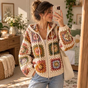 May include: A zip-up hooded jacket made of multi-colored crochet granny squares in shades of pink, yellow, green, and blue, featuring a cream-colored border, long sleeves, a front zipper closure, and a drawstring hood with cream-colored ties.