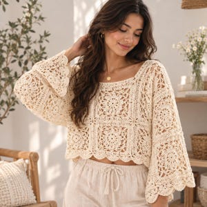 May include: A cream-coloured crochet top featuring a square-patterned design with intricate floral motifs, long bell sleeves, and a scalloped hemline. The garment is constructed from interconnected crochet squares, creating a textured, openwork appearance.