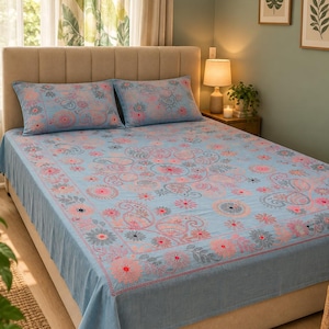 Può includere: Un set di lenzuola azzurro con un motivo ripetuto di fiori e disegni paisley in rosa e grigio scuro. Il set include due federe rettangolari abbinate e un grande lenzuolo che ricade sui lati della struttura del letto.