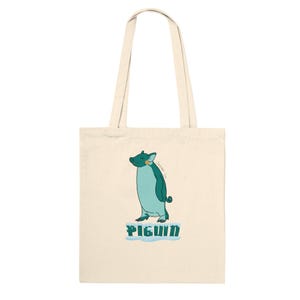 May include: A cream-colored canvas tote bag featuring a central graphic of a teal-colored hybrid creature that combines pig and penguin features. The creature stands on a light blue icy patch with the text PIGUIN printed in dark teal block letters below.