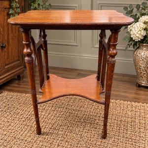 May include: A brown wooden side table featuring a rectangular top with rounded corners, four turned legs with vertical spindle supports, and a lower shelf with a cross-shaped design connecting the legs. The table has a smooth, polished finish.