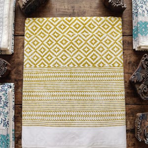 May include: A rectangular piece of fabric featuring a mustard yellow and white geometric diamond pattern on the top half, followed by horizontal stripes and chevron bands in the same colors, ending with a solid white border at the bottom.