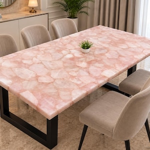 Puede incluir: Una mesa de comedor rectangular con un tablero compuesto por losas de cuarzo rosa pulido con un patrón de mosaico. La mesa está sostenida por una estructura de metal negro resistente con una base en forma de U y rodeada por seis sillas beige.