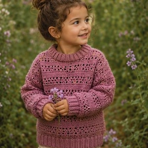 Peut inclure: Un pull à manches longues mauve présentant un motif en crochet texturé avec des bandes horizontales de points ajourés, un col rond côtelé et des poignets côtelés. Le vêtement est porté avec un short de couleur claire, créant un ensemble.