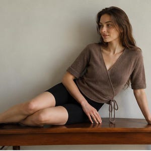 Può includere: Un top a portafoglio in maglia marrone con maniche corte e chiusura con laccetti laterali, abbinato a pantaloncini neri aderenti. Il top presenta uno scollo a V e una finitura testurizzata, mentre i pantaloncini sono neri e arrivano a metà coscia.