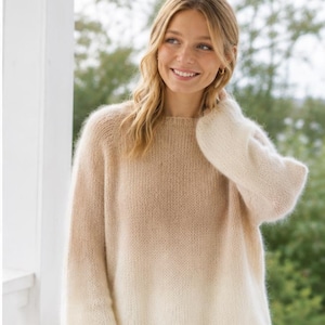 Könnte beinhalten: Ein langärmeliger Pullover mit Rundhalsausschnitt, weicher, flauschiger Textur und einem Farbverlauf, der von einem warmen Beige oben zu einem cremigen Off-White unten übergeht, gefertigt mit lockerer Passform und geripptem Halsausschnitt.
