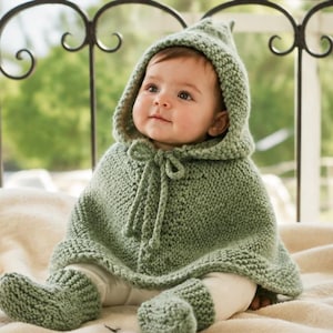 May include: A sage green knitted baby poncho with an attached hood and a matching pair of knitted booties. The poncho features a textured garter stitch pattern and a central drawstring tie closure at the neckline, crafted from soft yarn.